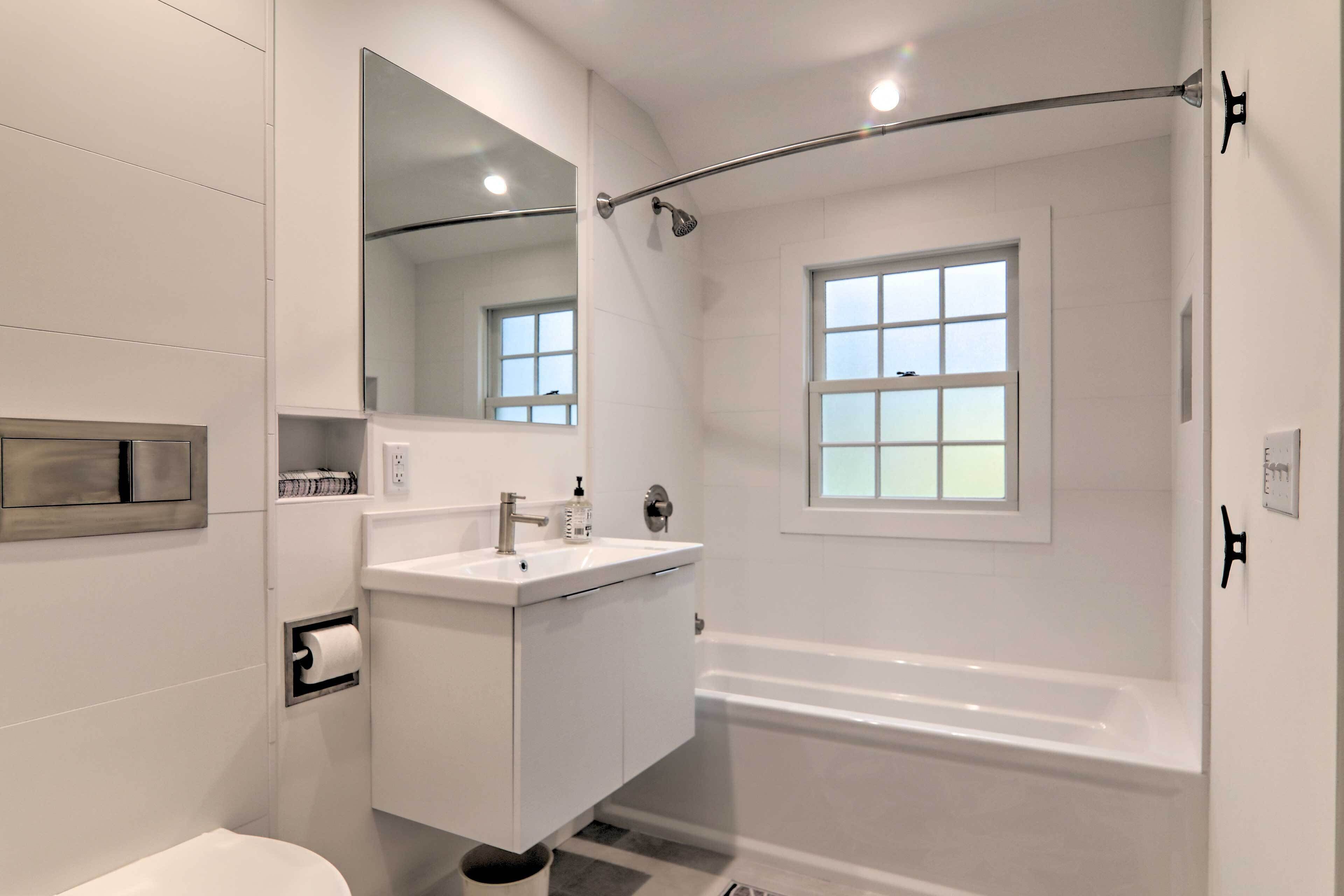 A modern bathroom with a white sink, mirror, and bathtub.