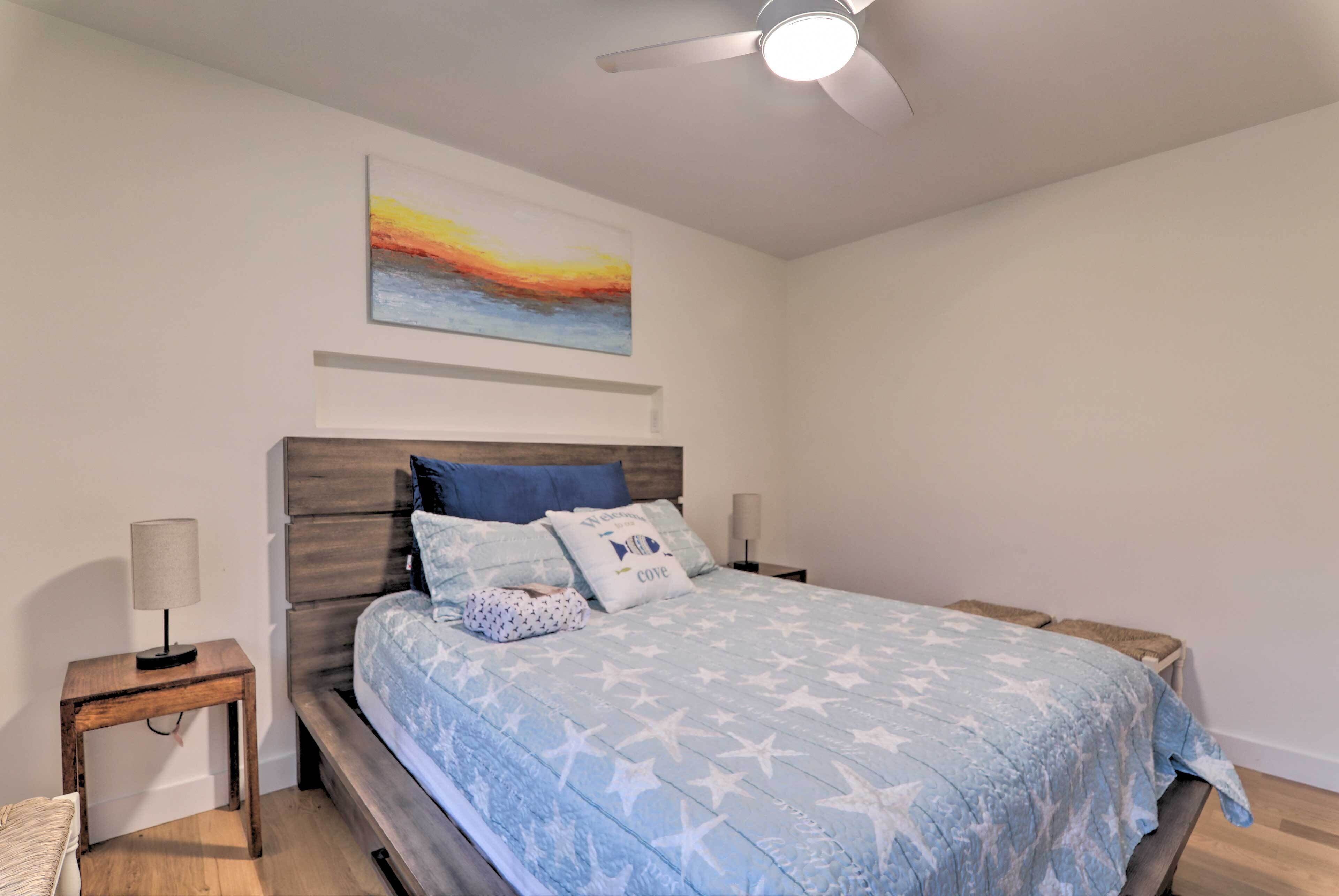 Een slaapkamer met een bed, nachtkastje, lamp, plafondventilator en een schilderij aan de muur.