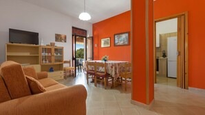 A living room with a sofa, TV, and wooden cabinets. There is a dining area with a table and chairs. - 3337 Residence Garden Sea - PP by Barbarhouse (Porto Cesareo)