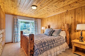 A wooden-paneled bedroom with a bed, a nightstand, a dresser, and a window with curtains.