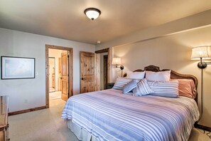 A bedroom with a large bed, two bedside lamps, and a door leading to another room.