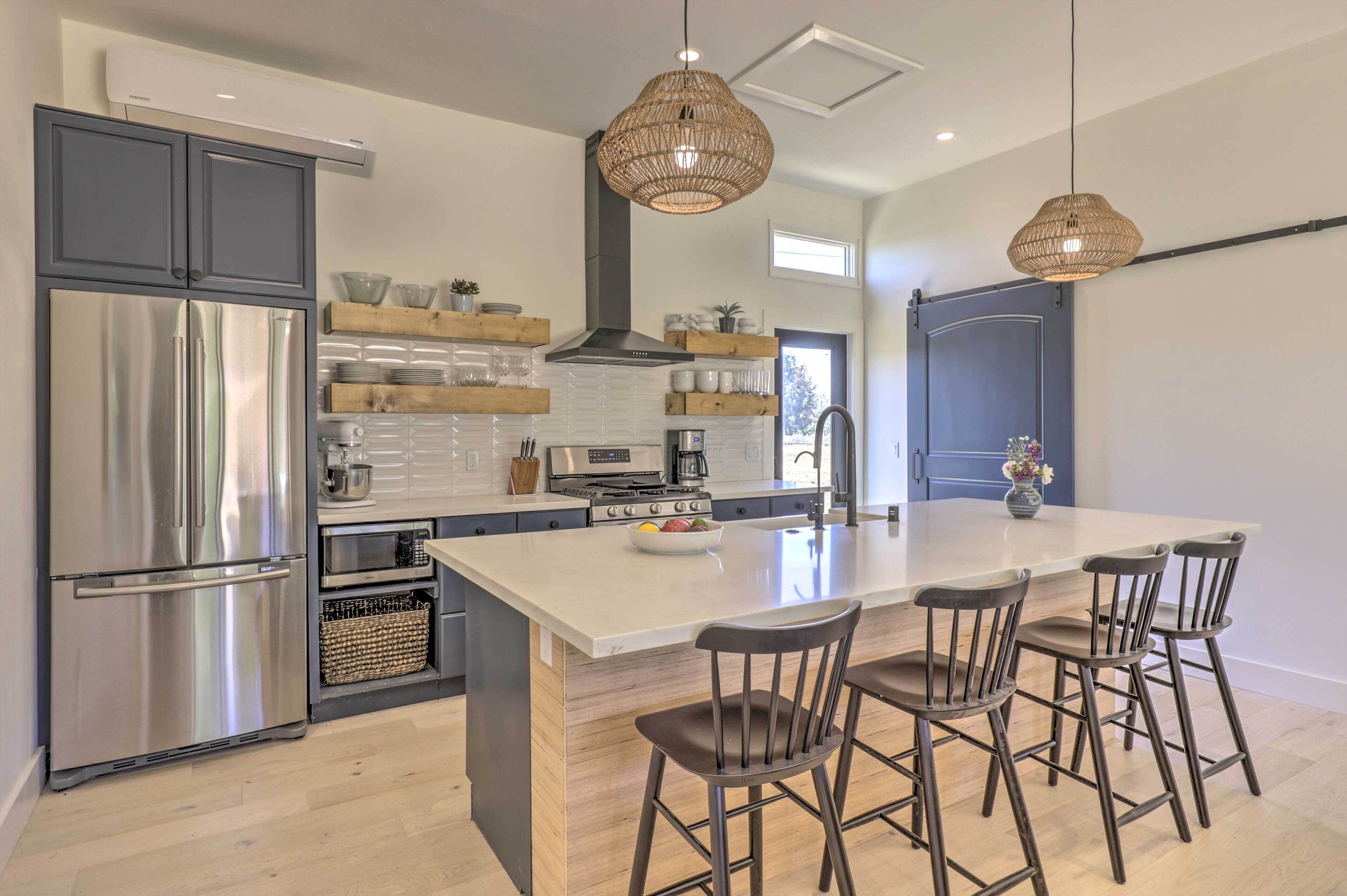A modern kitchen with a large island, stainless steel appliances, and wicker pendant lights.