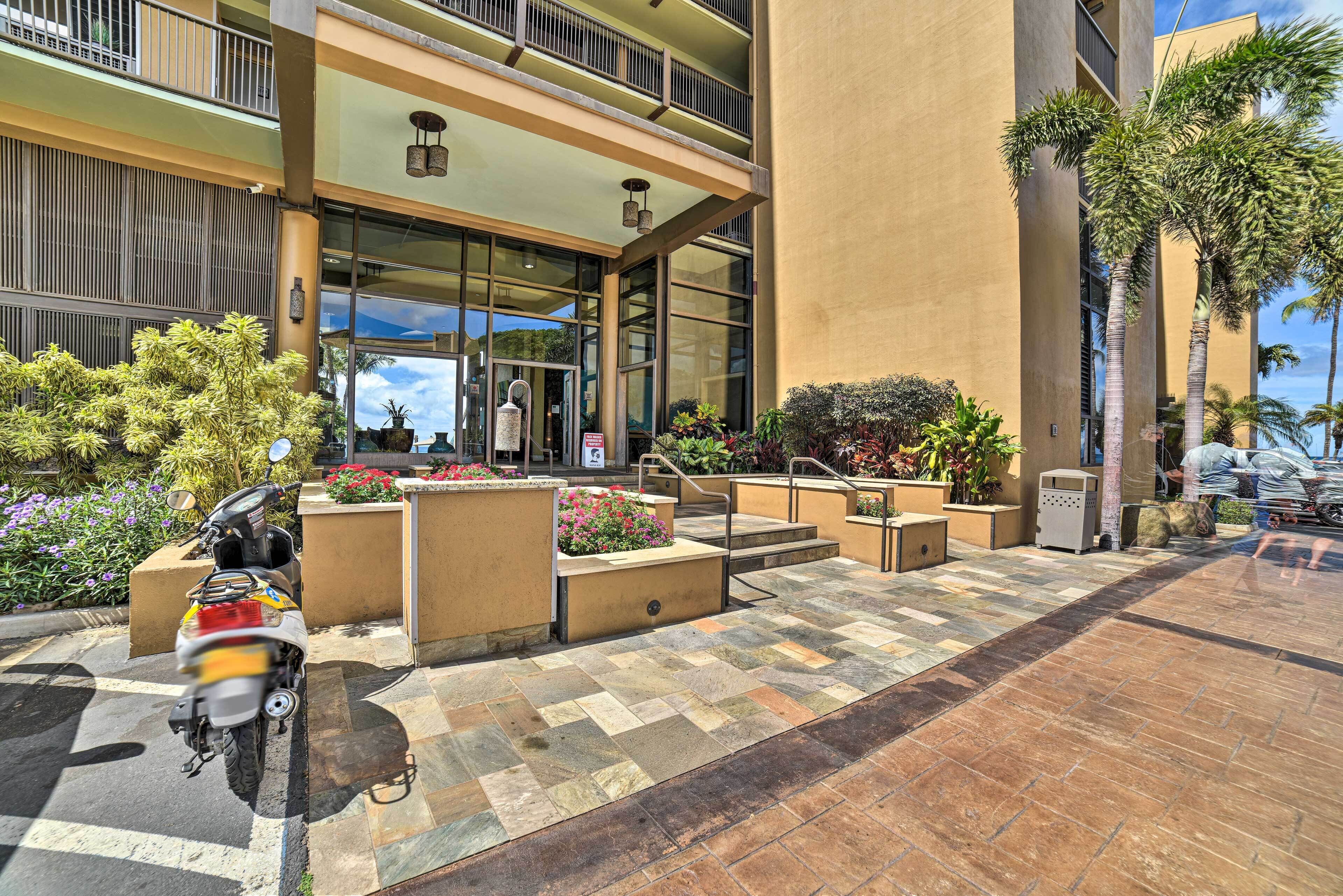 A multi-story building with a paved entrance area, outdoor seating, and a parked scooter.