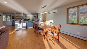 Amplia sala de estar con una mesa de comedor de madera, sillas, cocina y un ventanal grande.