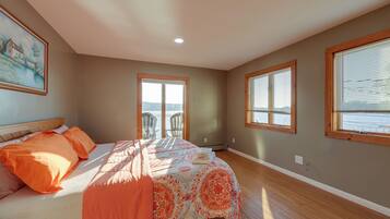 A bedroom with a bed, two chairs, a painting, and a view of the outdoors.