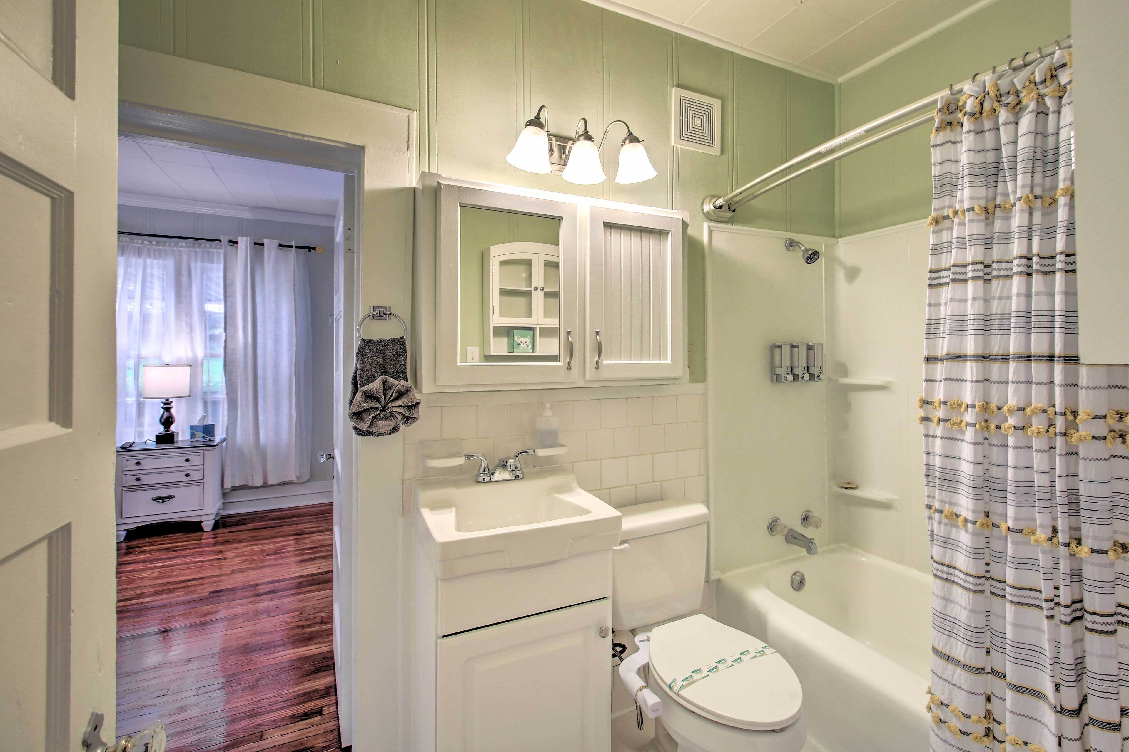 A bathroom with a white sink, toilet, and bathtub. There is a mirror above the sink and a shower curtain with a pattern.