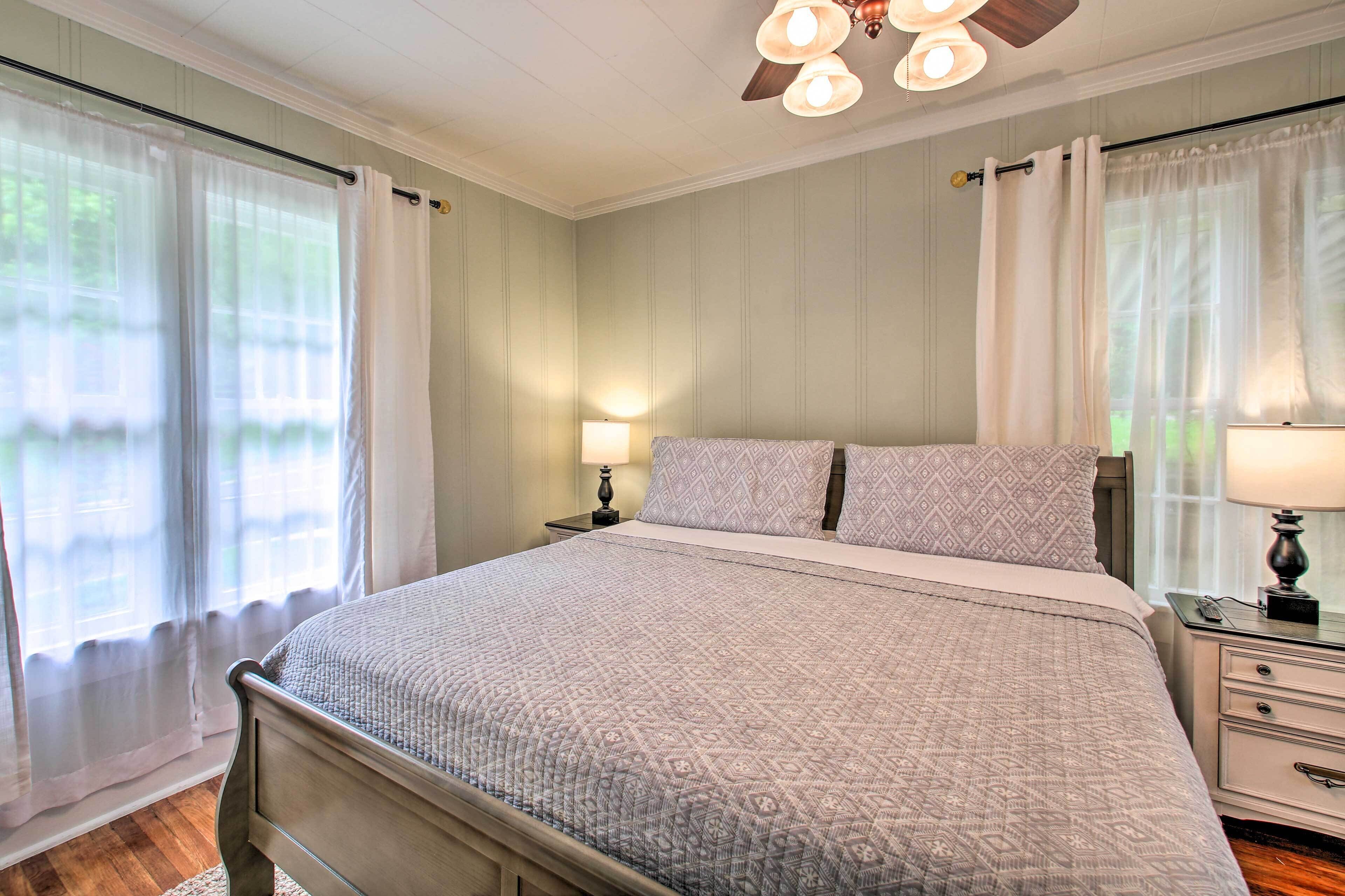 A neatly made bed with a patterned bedspread, a bedside table with a lamp, and a window with sheer curtains.
