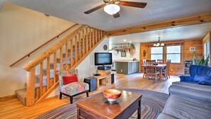 A spacious living room with a wooden staircase, a television, a dining area, and a large window. - The Pinecone Palace w/ Hiking Trail Access! (Lyons)