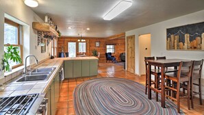 A kitchen with a central island, a dining area with wooden chairs, and a large rug. - The Pinecone Palace w/ Hiking Trail Access! (Lyons)