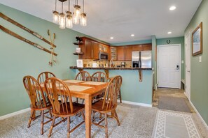 A dining area with a wooden table and chairs, a kitchen with wooden cabinets, a microwave, and a refrigerator.