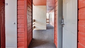 Un couloir aux murs en bois rouge et au sol recouvert d’une moquette, qui mène à une porte blanche.