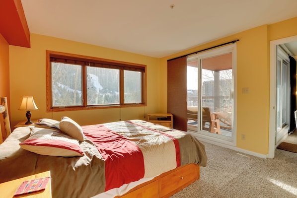 A bedroom with a large window, a bed, a nightstand, and a sliding glass door leading to an outdoor area.