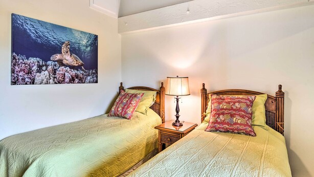 Ein Doppelbett mit zwei Kissen, ein Nachttisch mit Lampe und ein gerahmtes Bild einer Meeresschildkröte an der Wand.