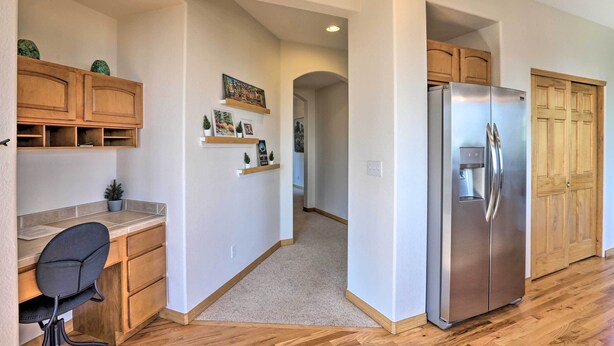 A kitchen with wooden cabinets, a stainless steel refrigerator, a desk with a chair, and a hallway leading to another room. - Spacious Evergreen Home w/ Picturesque Views (Evergreen)