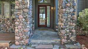 A stone pillar entrance with a red door and a welcome mat. - Spacious Evergreen Home w/ Picturesque Views (Evergreen)