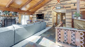 Ein rustikales Interieur mit Kamin aus Stein, Holzbalken, einem grauen Modulsessel und einer Bar aus Holz.