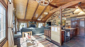 Ein großzügiger Wohnbereich mit Kamin, eine Küche mit dunklem Steinboden und Holzbalken an der Decke.