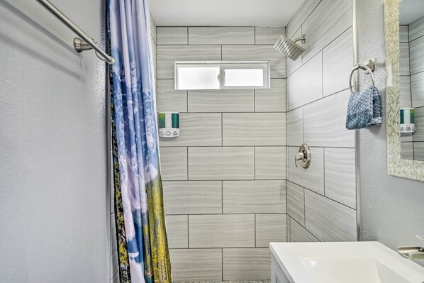 A bathroom with a shower, a window, a towel rack, and a sink.