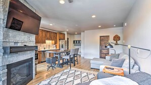A modern living room with a stone fireplace, a dining area with wooden cabinets, and a cozy seating area with a sofa and a coffee table. - 3 Mi to Dillon Reservoir: Condo w/ Balcony! (Silverthorne)