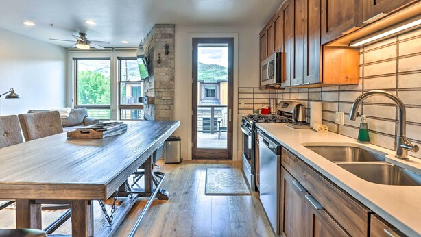 A modern kitchen with wooden cabinets, stainless steel appliances, and a large dining table. - 3 Mi to Dillon Reservoir: Condo w/ Balcony! (Silverthorne)