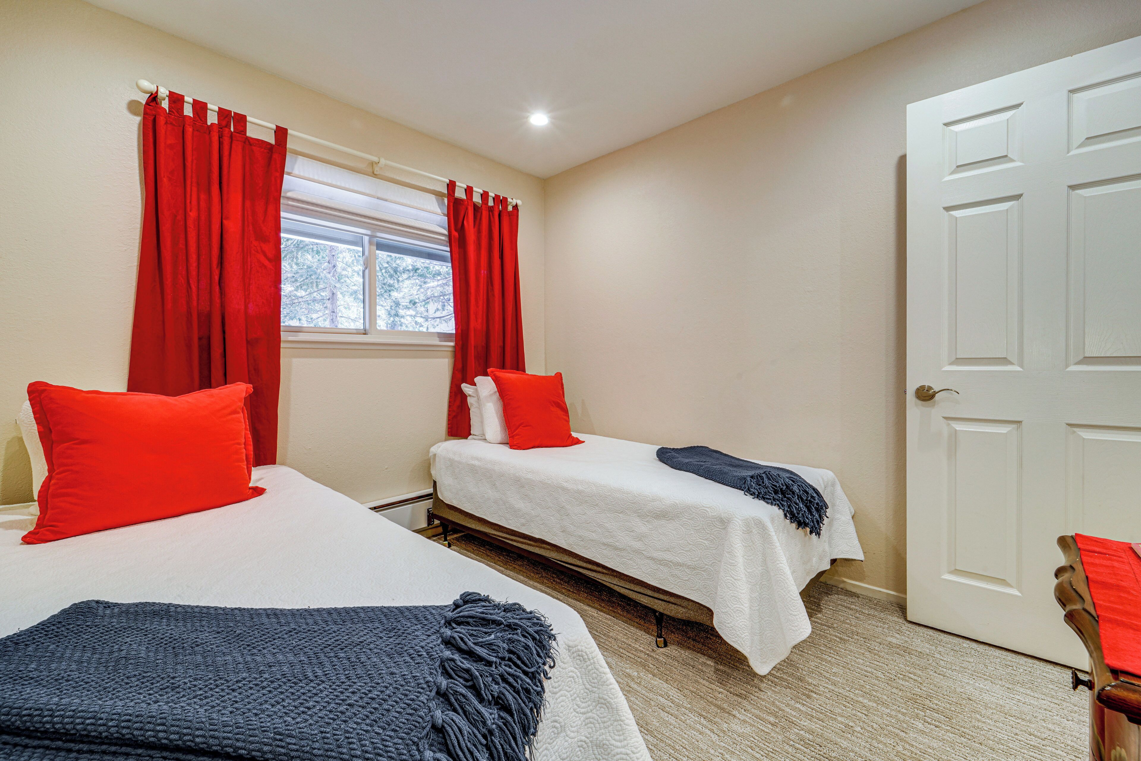 Two single beds with red and white bedding, a window with red curtains, and a white door.