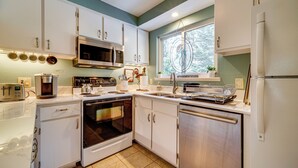 A modern kitchen with white cabinets, stainless steel appliances, and a window with a view of trees. - Artists Tahoe Retreat: Pool, Art & Ski Access! (Incline Village)