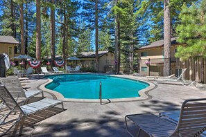 A swimming pool with lounge chairs and a fence, surrounded by tall trees.