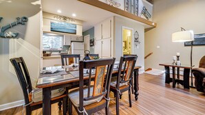A dining area with a wooden table and chairs, a kitchen in the background, and a staircase leading to an upper level. - Artists Tahoe Retreat: Pool, Art & Ski Access! (Incline Village)