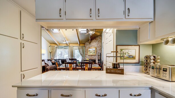 A kitchen with white cabinets, a marble countertop, and a dining area with a table and chairs. - Artists Tahoe Retreat: Pool, Art & Ski Access! (Incline Village)