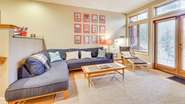 A living room with a sectional sofa, a coffee table, and a side table with a lamp. There are framed pictures on the wall and a window with blinds. - Lake Tahoe Corner Condo w/ Hot Tub, Beaches Nearby (Incline Village)