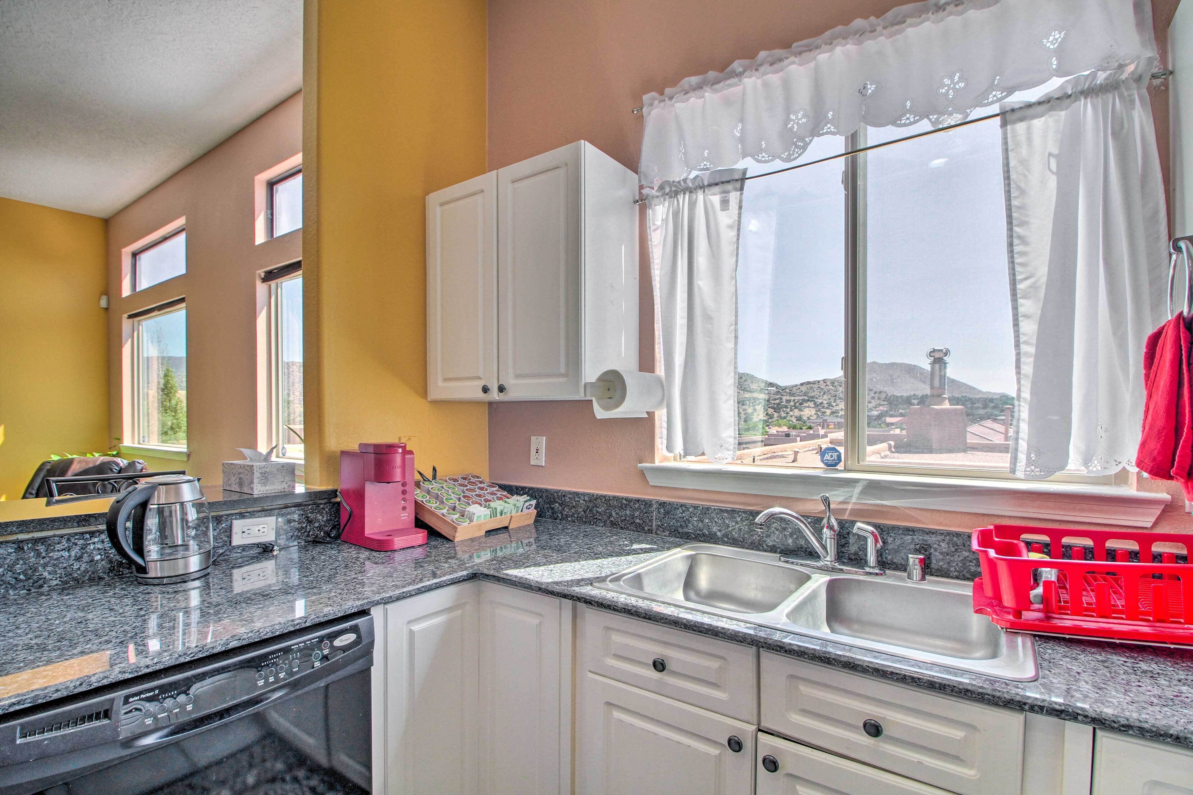 A kitchen with a dishwasher, a coffee maker, and a window with curtains.