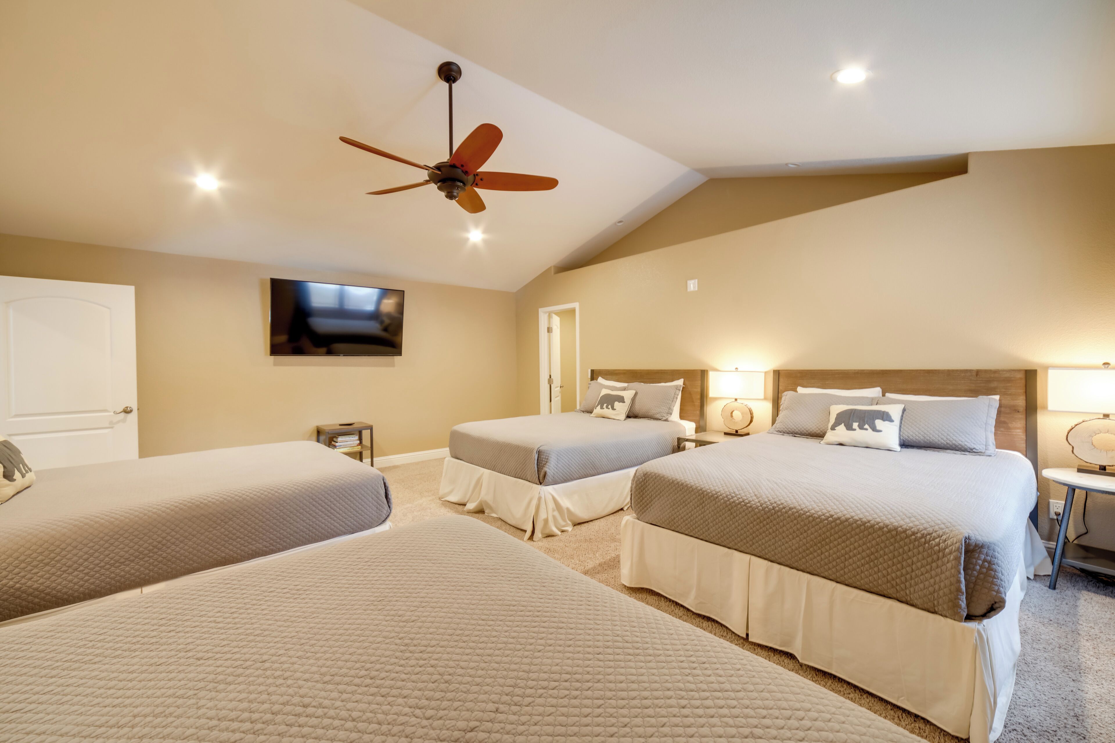 A hotel room with three beds, a ceiling fan, and a TV mounted on the wall.