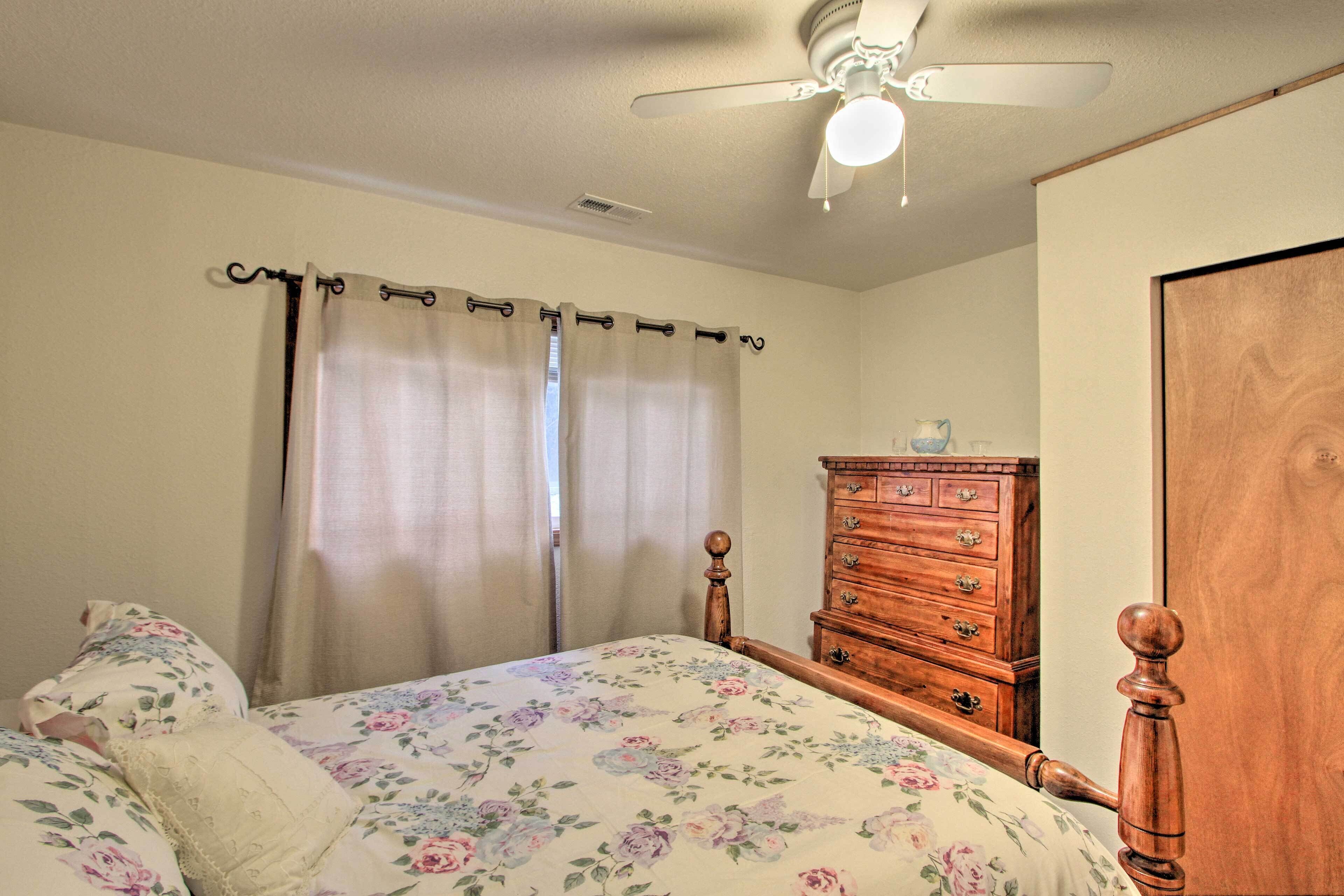 A bedroom with a bed, a wooden dresser, a ceiling fan, and a window with curtains.