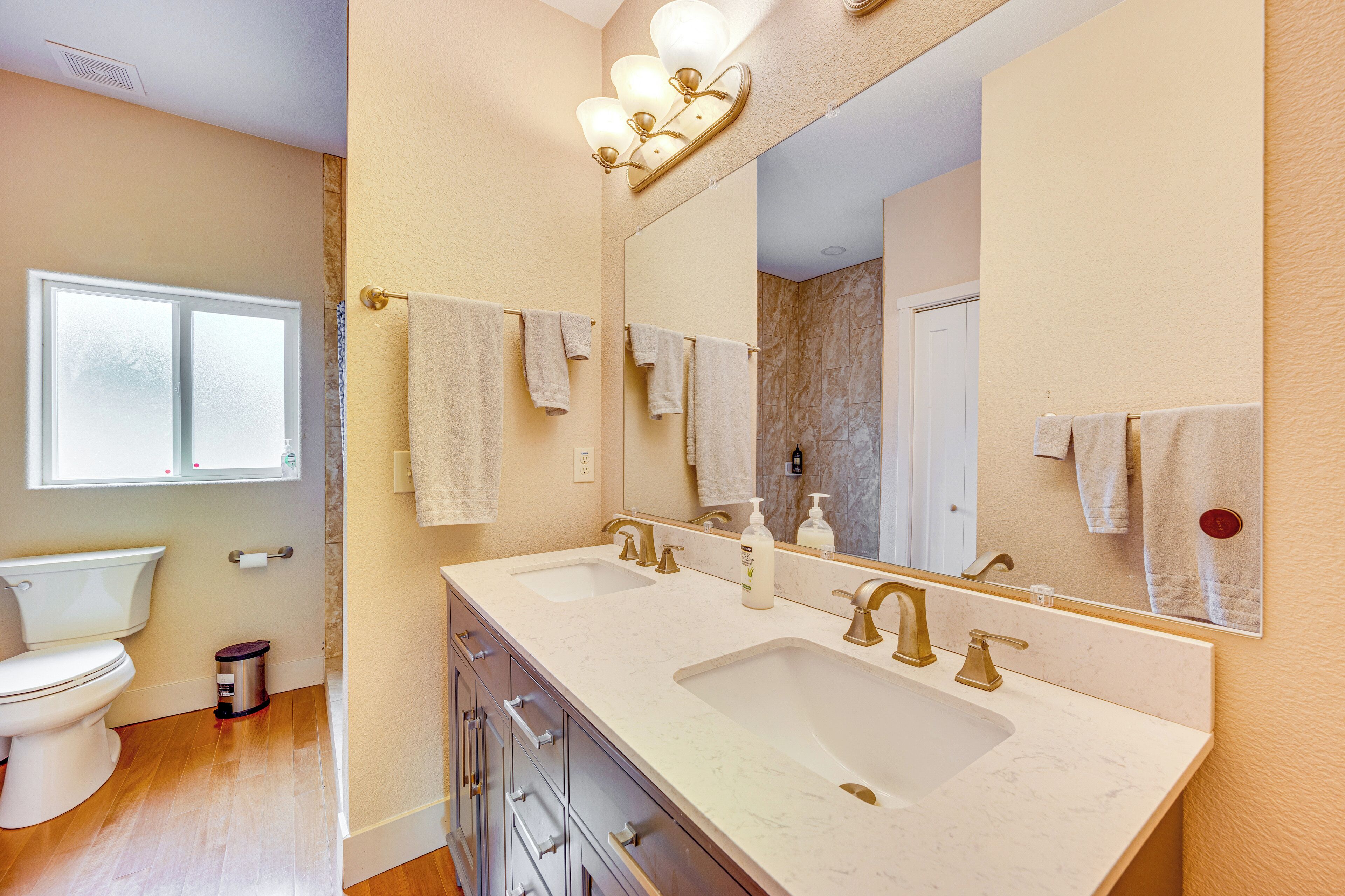 A bathroom with a dual sink vanity, a toilet, and a large mirror.
