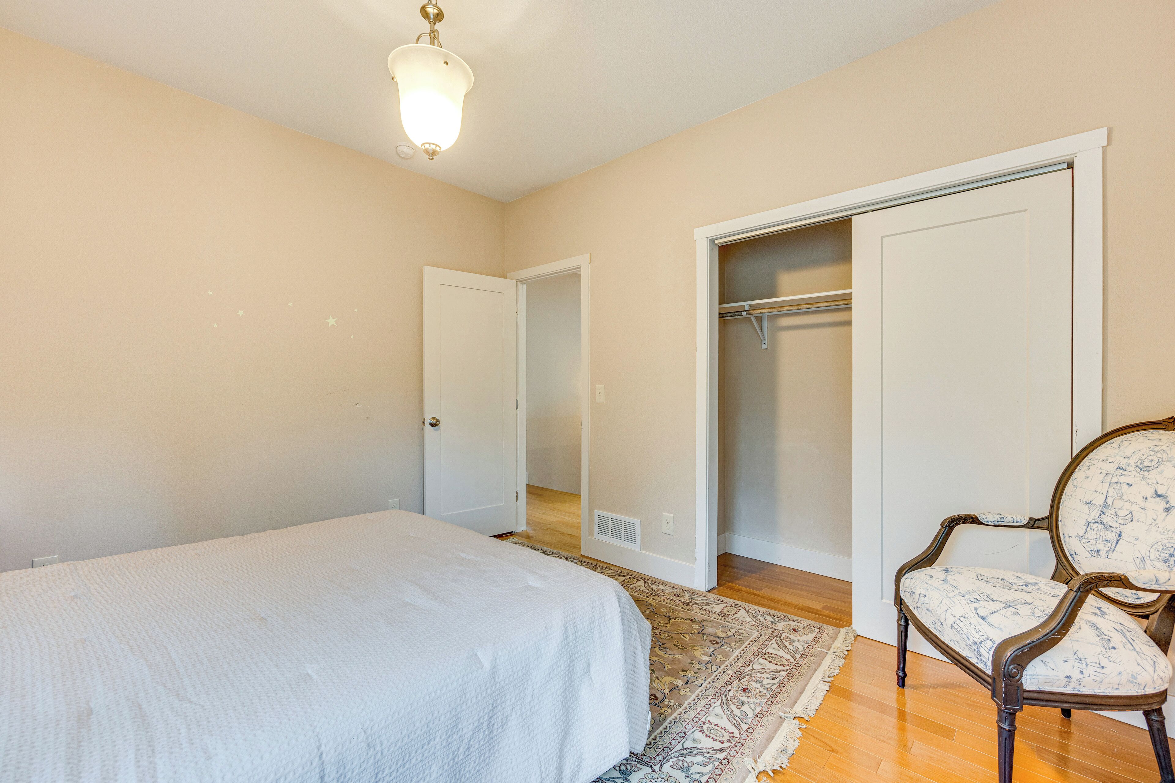 A bedroom with a bed, a chair, a closet, and a hallway.