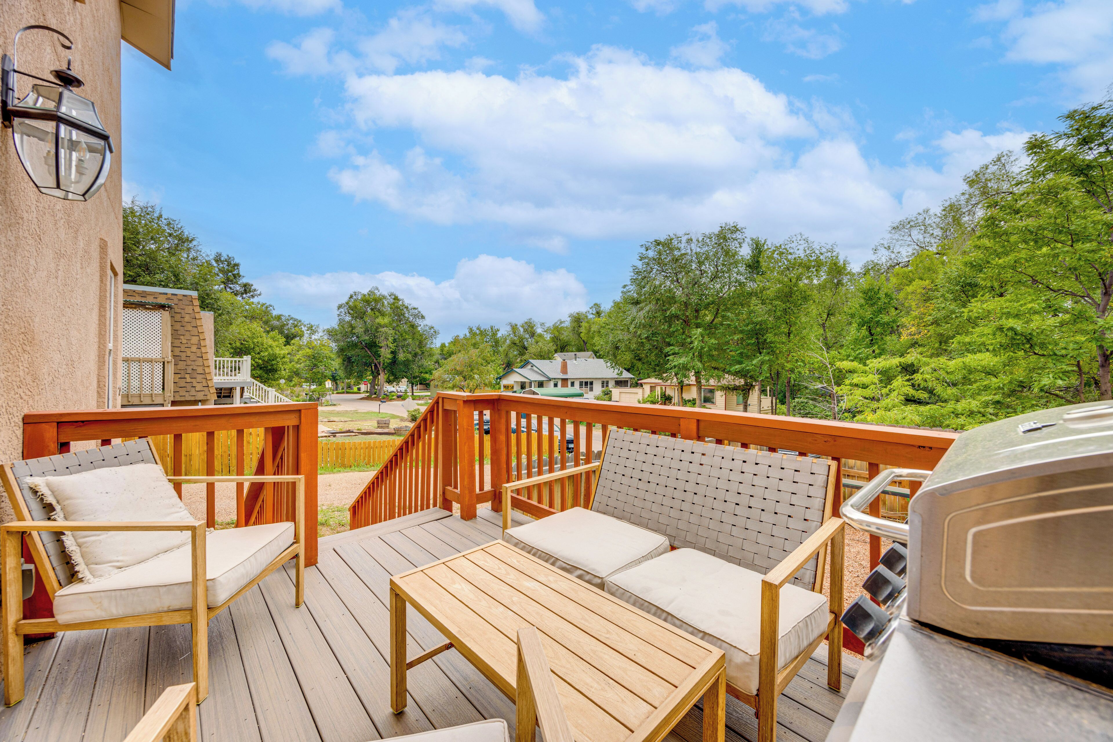A wooden deck with outdoor furniture, a barbecue grill, and a view of a residential area.