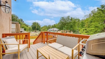 A wooden deck with outdoor furniture, a barbecue grill, and a view of a residential area.