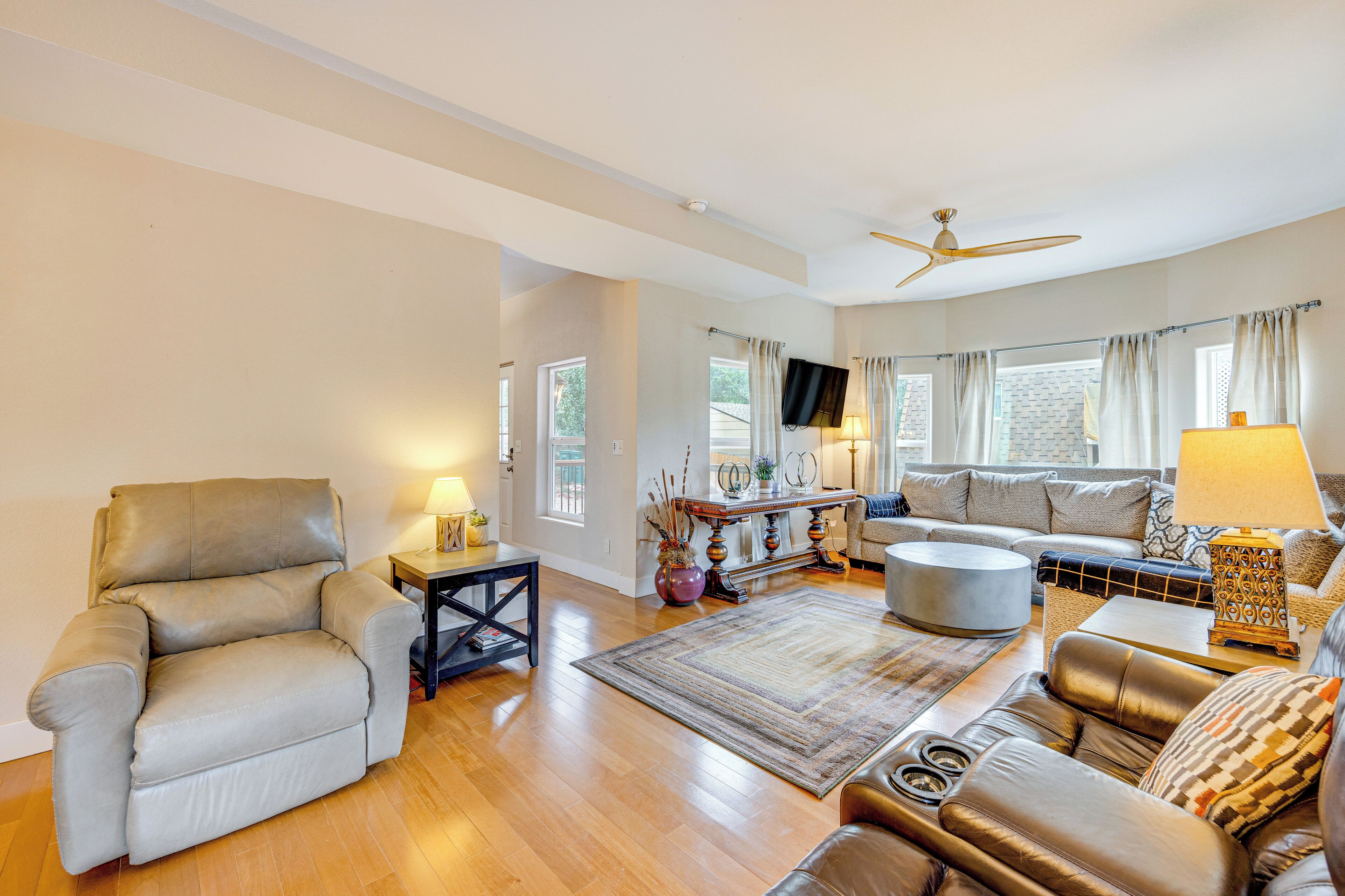 A spacious living room with a leather sofa, a coffee table, and a TV mounted on the wall.