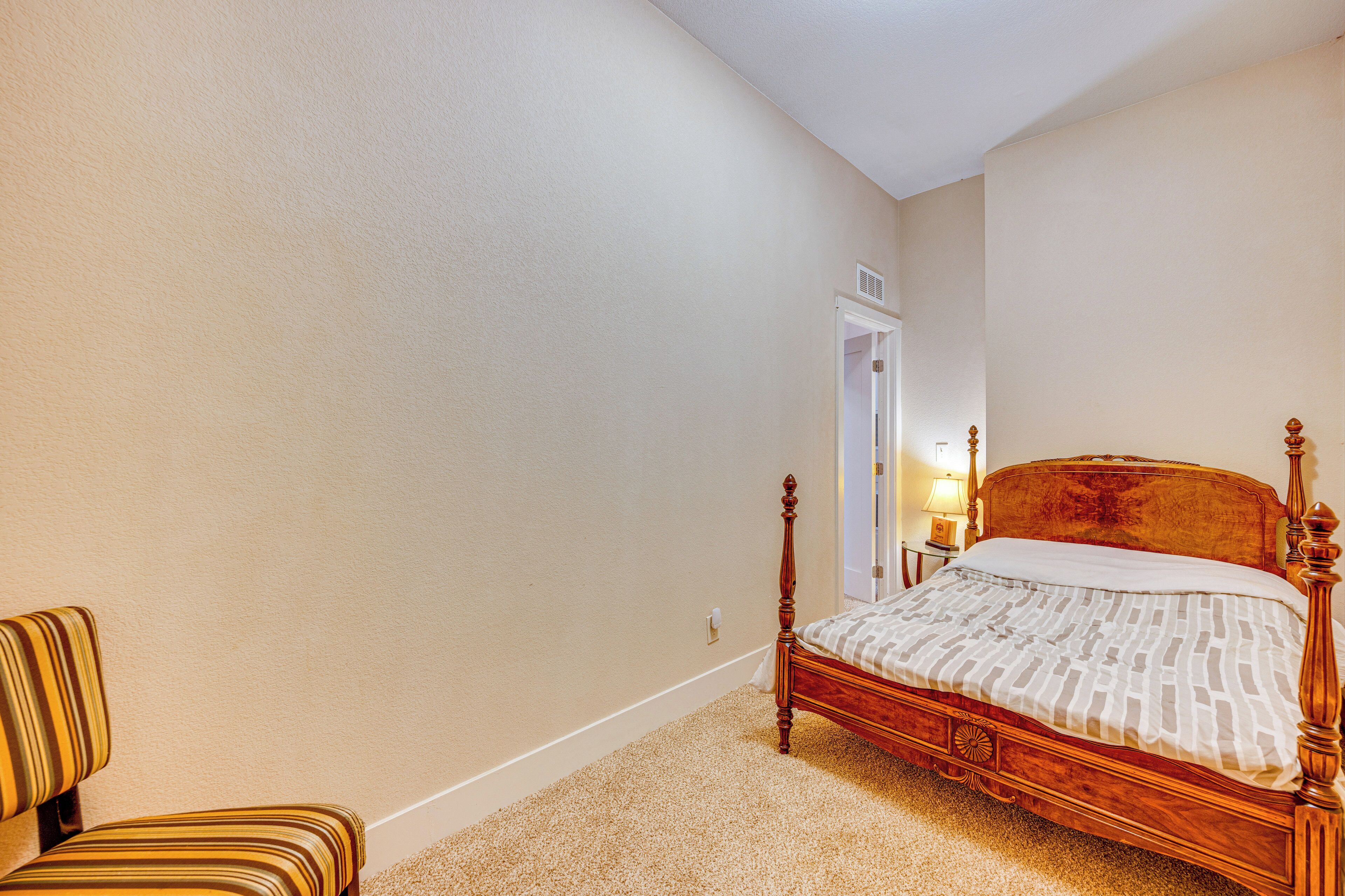 Un dormitorio con una cama de madera, una silla a rayas y suelo alfombrado.
