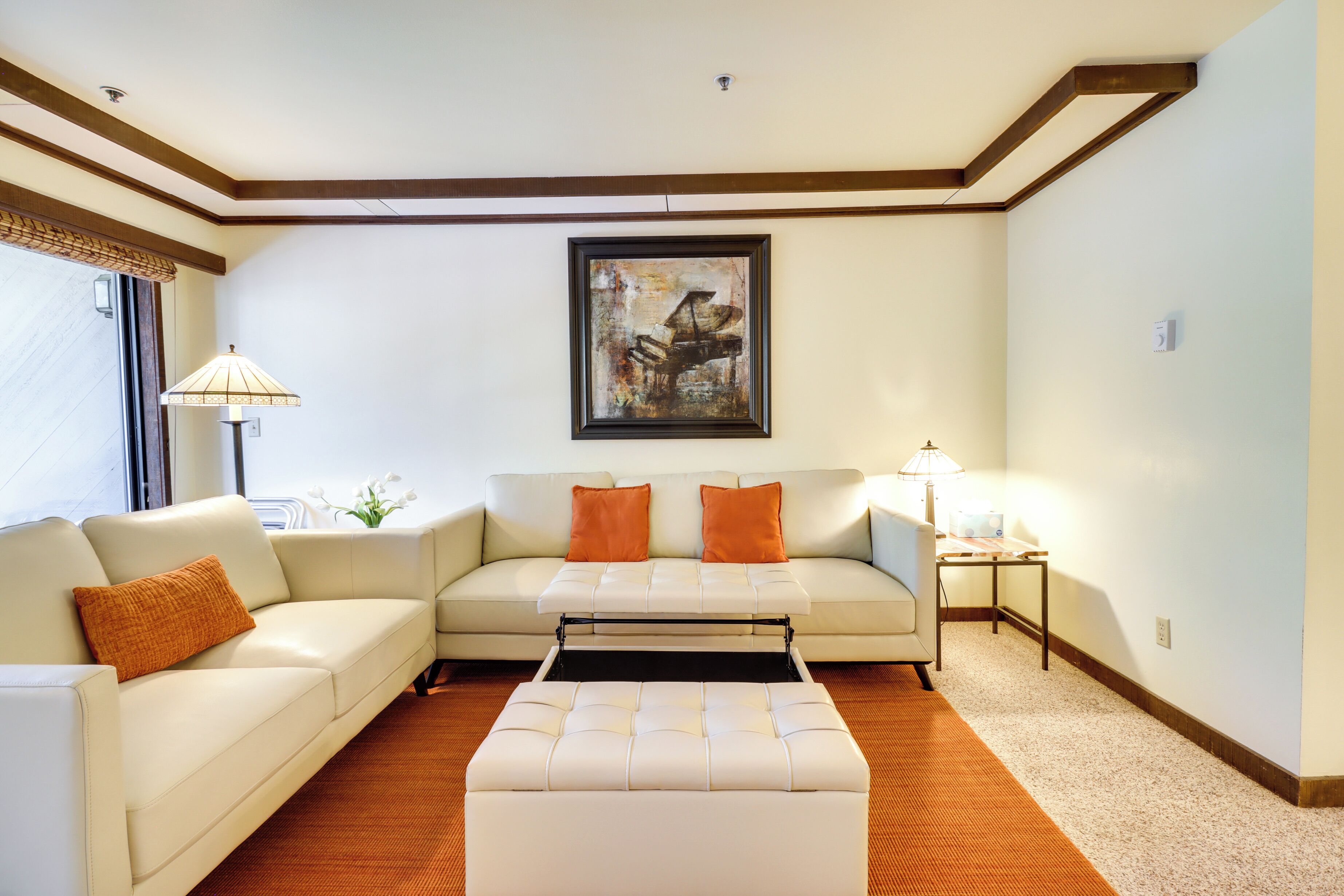A living room with a sofa, ottoman, and a painting on the wall.