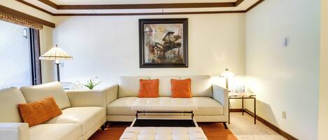 A living room with a sofa, ottoman, and a painting on the wall.