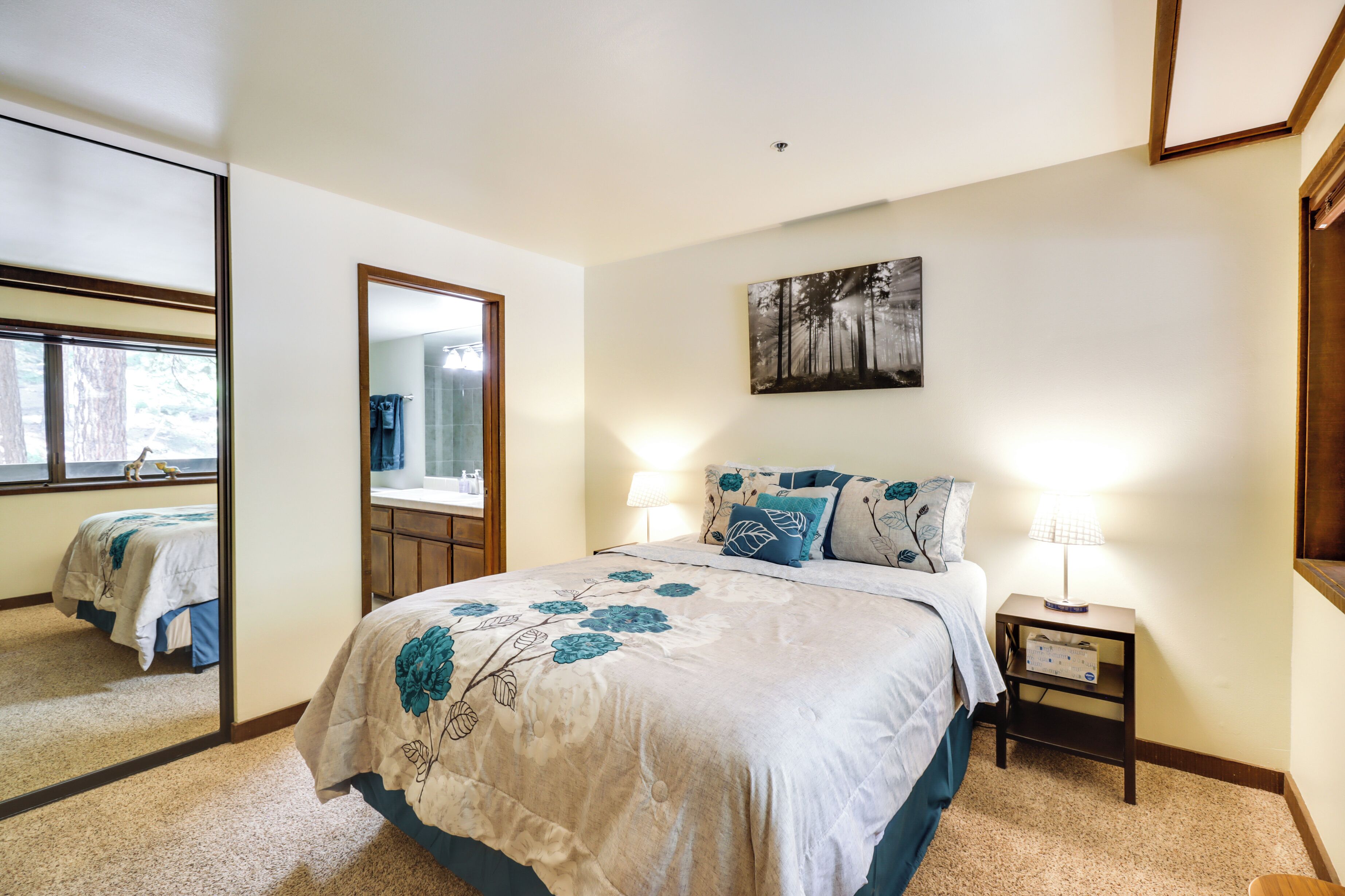 A bedroom with a large bed, a bedside table with a lamp, a mirror, and a painting on the wall.
