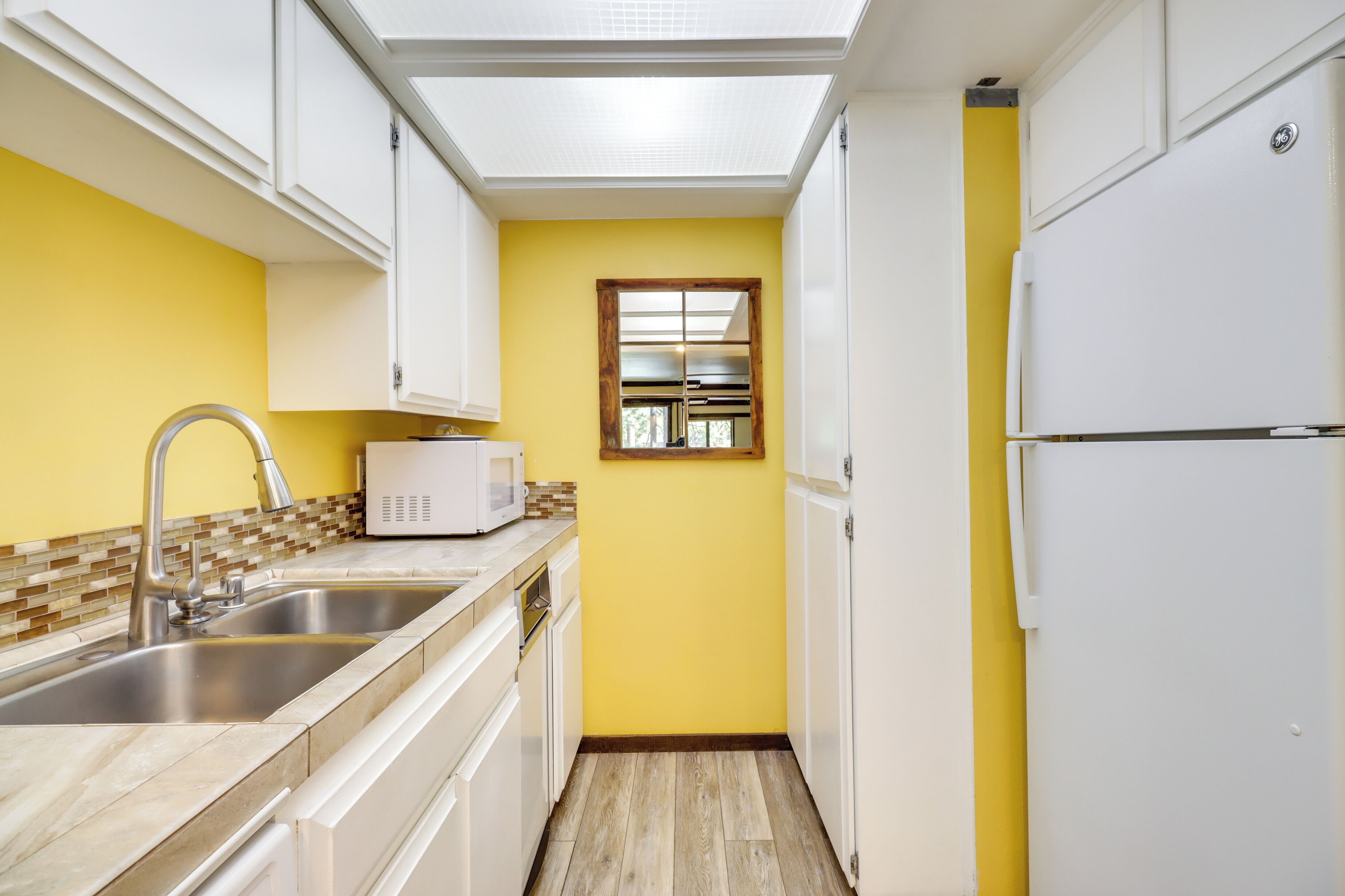 A narrow kitchen with white cabinets, a microwave, and a refrigerator.