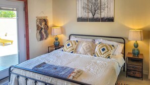 A neatly arranged bedroom with a bed, two bedside tables, a wall-mounted lamp, and a door leading to an outdoor area.