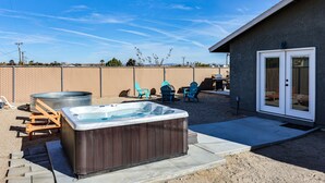 A backyard with a hot tub, outdoor seating, and a covered patio area.