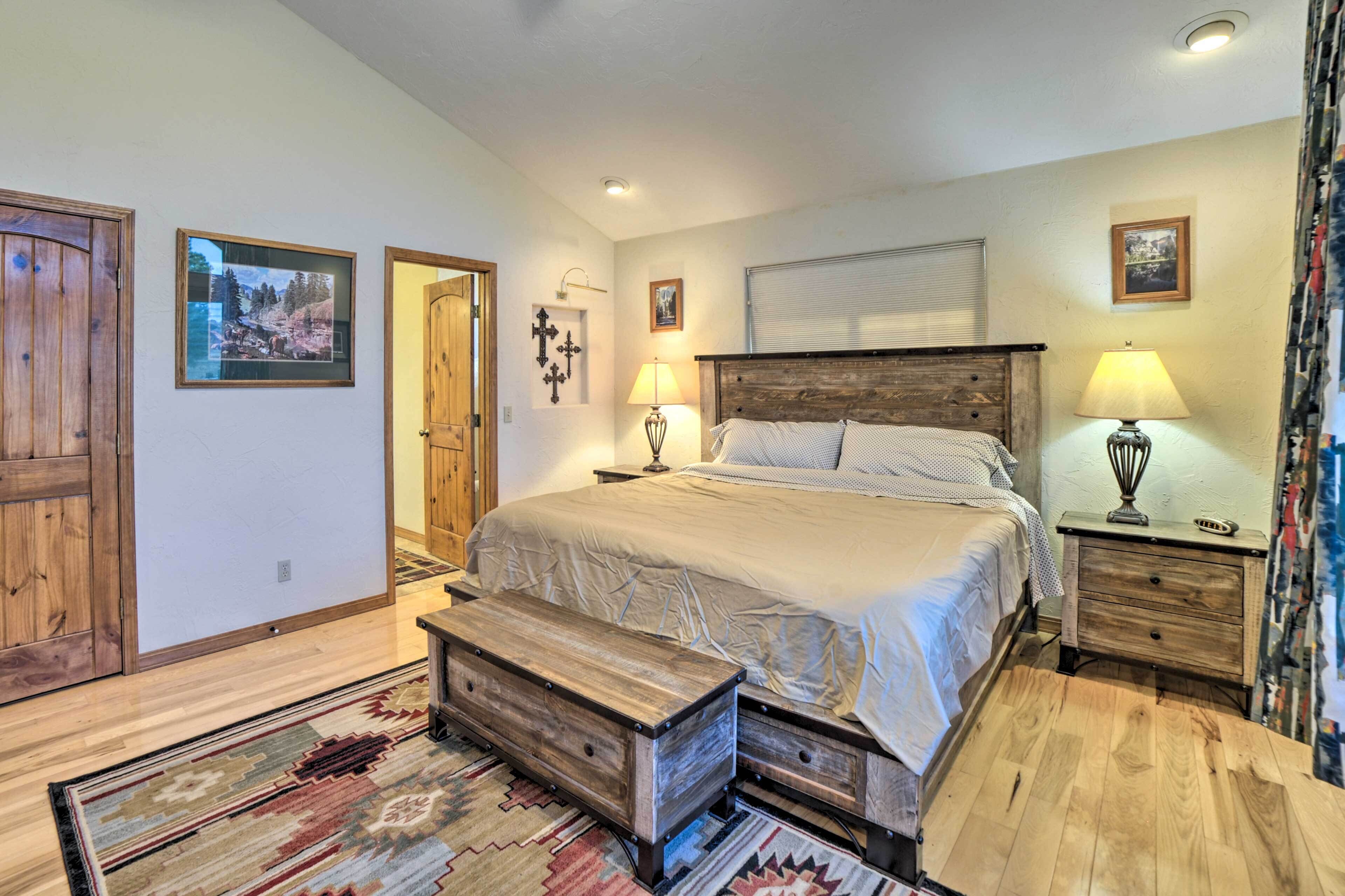 A bedroom with a large bed, wooden headboard, bedside tables, a bench, and a patterned rug.