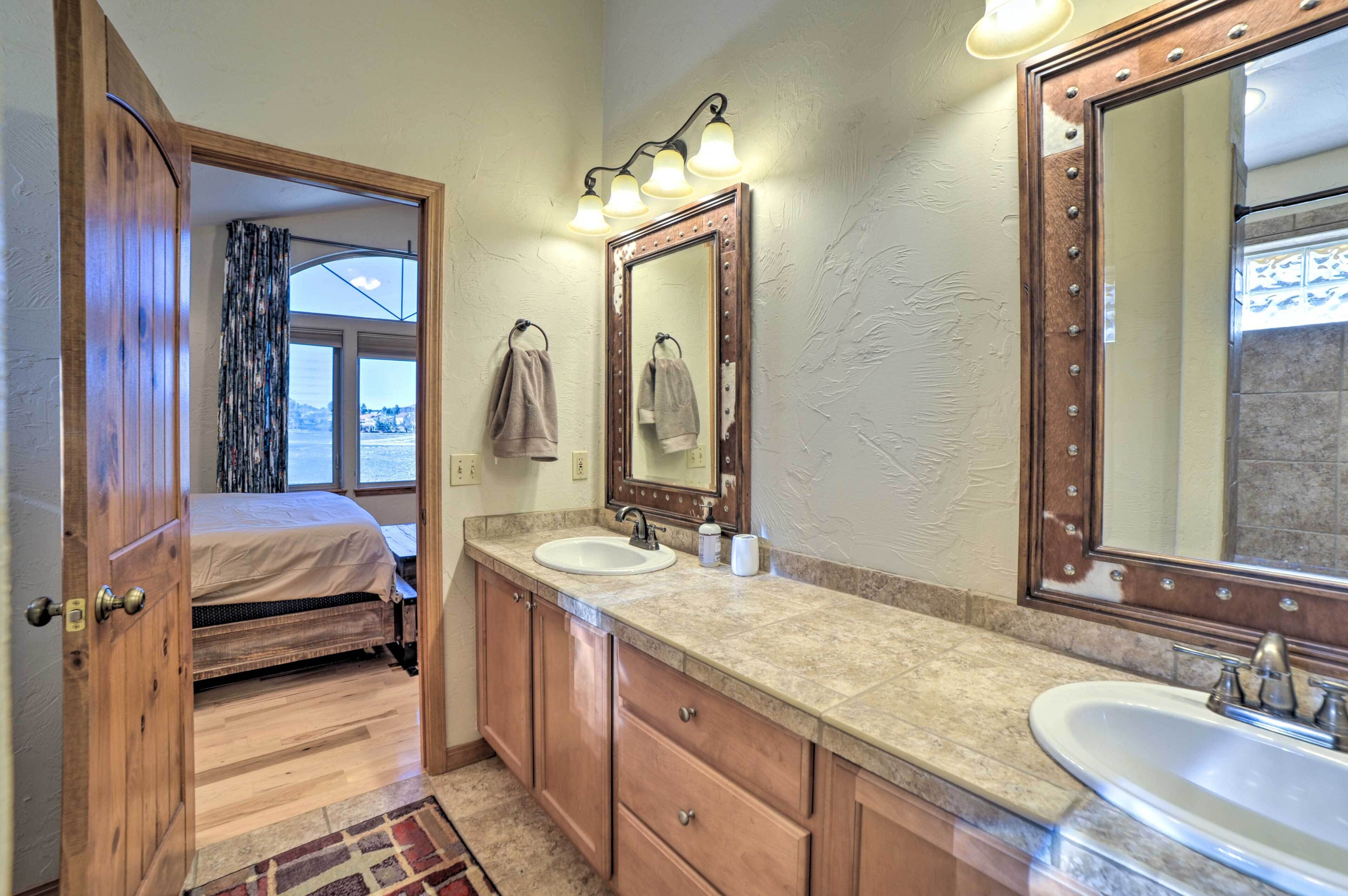 A bathroom with a wooden door, a bed, a large mirror, and a sink.