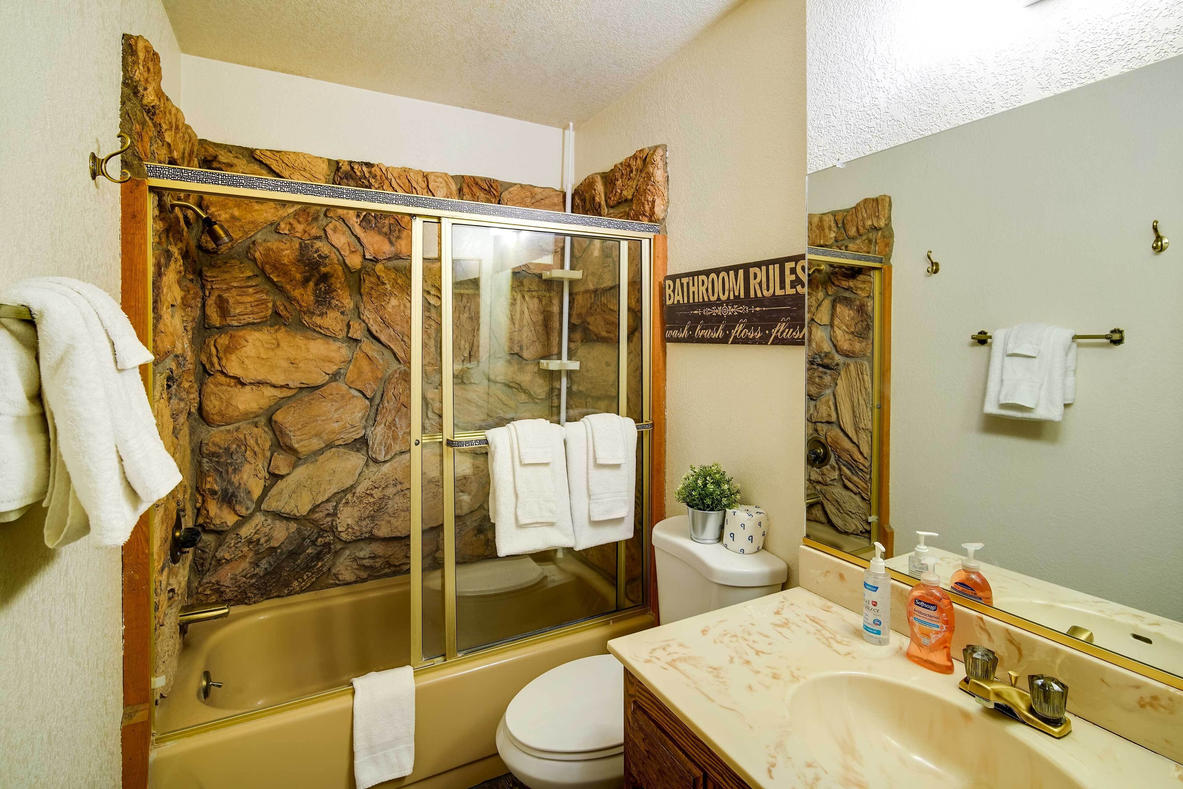Une salle de bain avec un mur en pierre, une douche en verre, des toilettes, un lavabo avec un plan de toilette en marbre et un miroir.