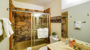 A bathroom with a stone wall, a glass-enclosed shower, a toilet, a sink with a marble countertop, and a mirror.