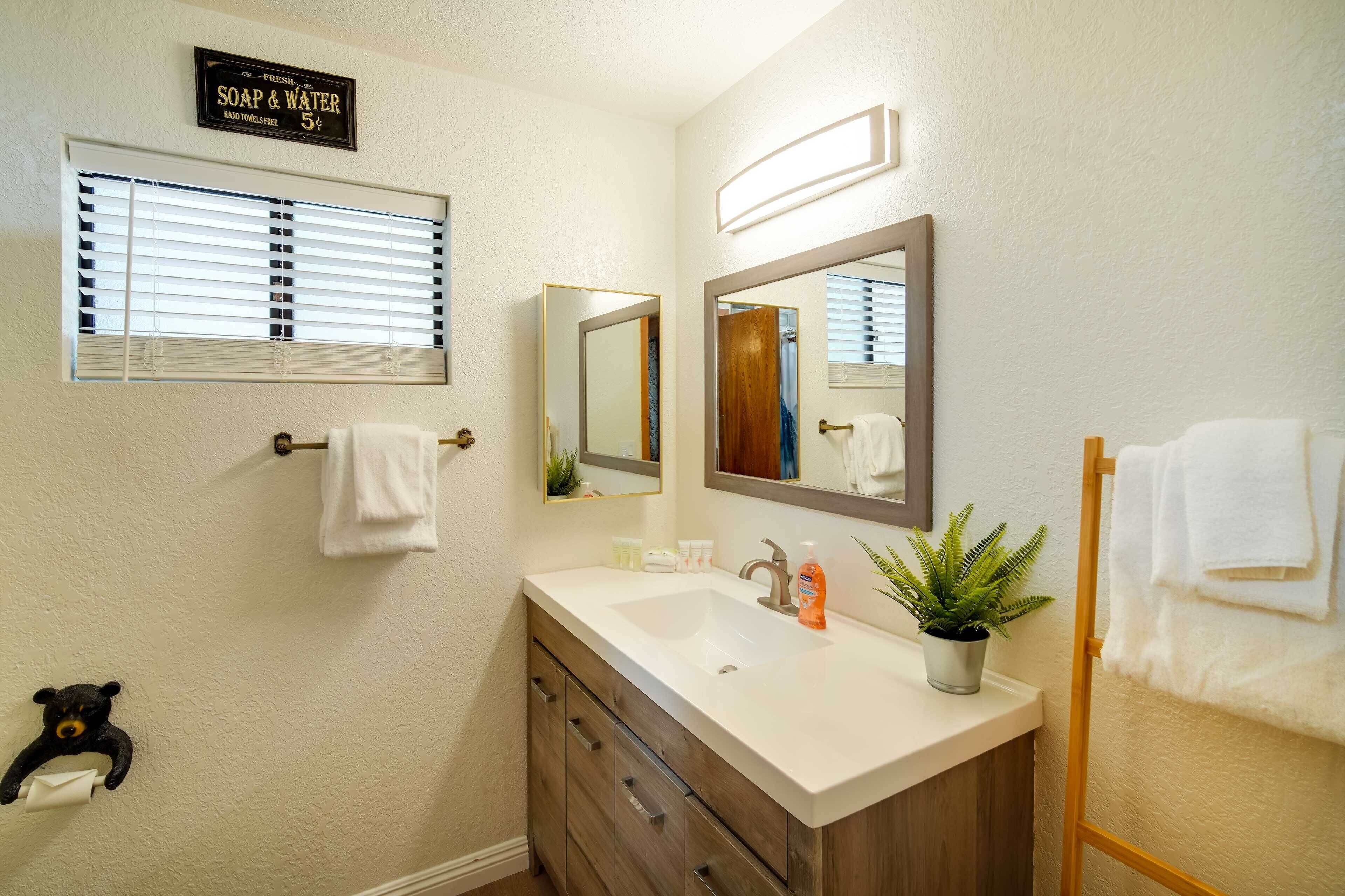 A bathroom with a white sink, wooden vanity, a mirror, a towel rack, and a sign for free soap and water.
